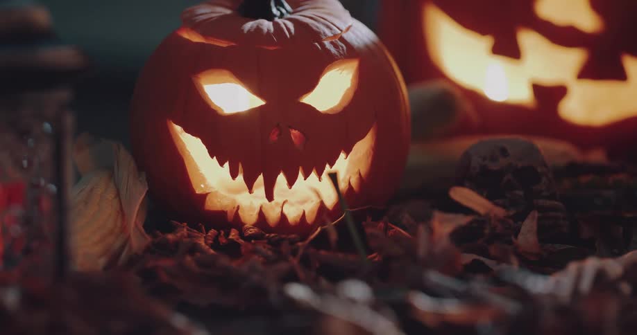 Two flame flame lit jack o lanterns sit on the ground near a burning lantern