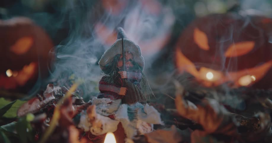 Carved pumpkins sit outside in leaves with decorations as smoke rises