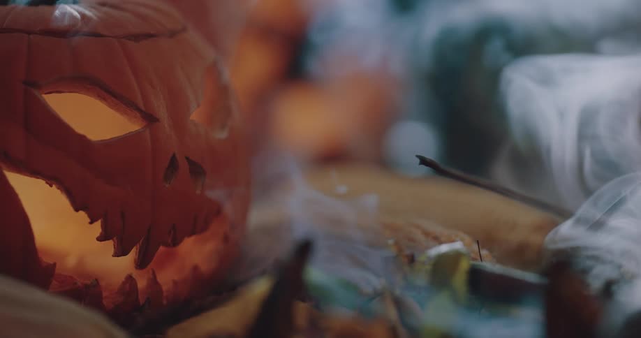 Halloween pumpkin sitting over dry leaves surrounded by white smoke