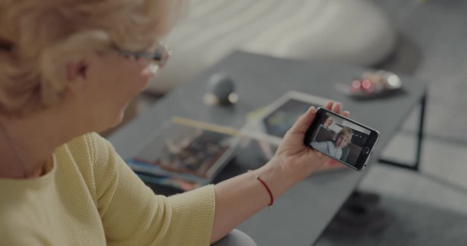 Grandmother interacts with grandson over mobile phone video call while sitting in living room