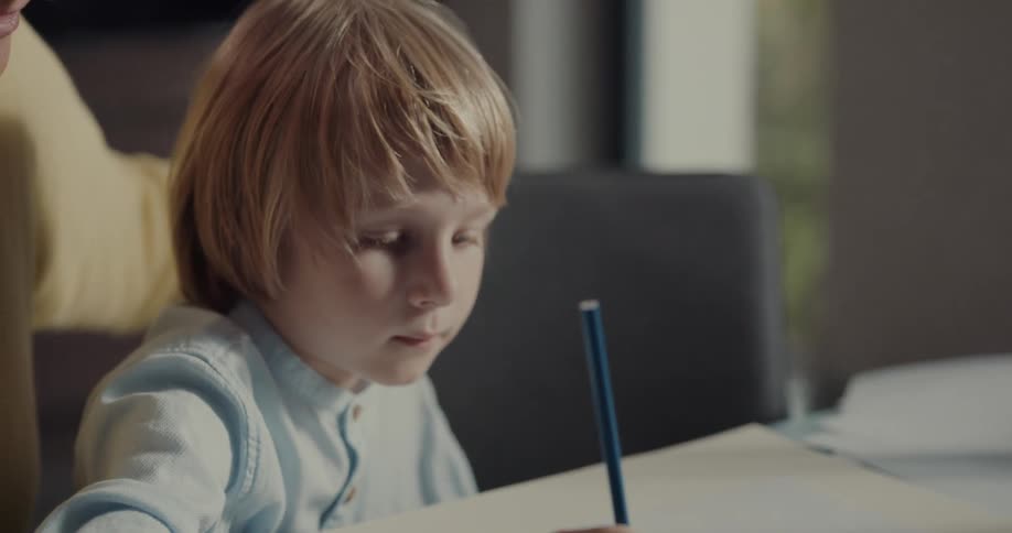 A boy draws while sitting at a paper covered with colored pencils