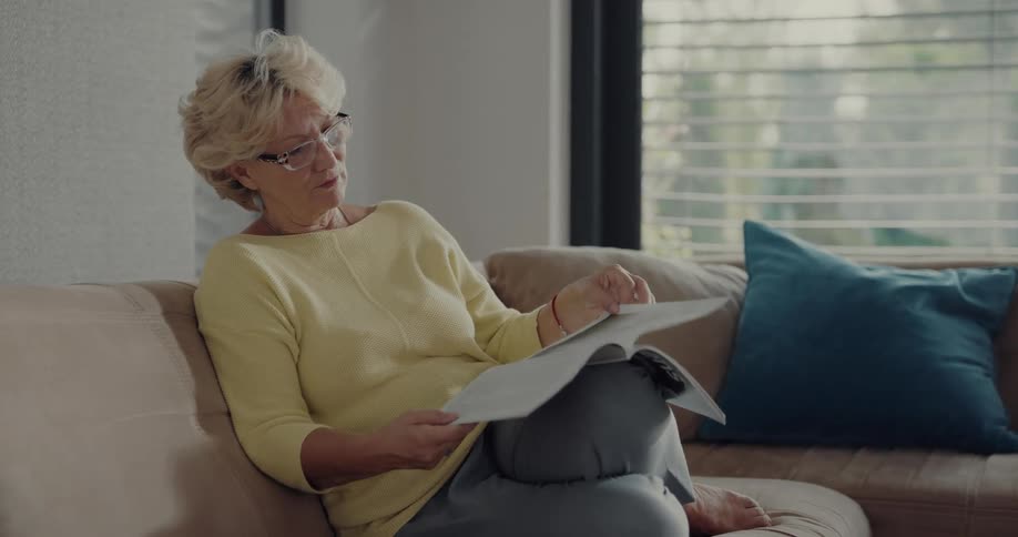 Female senior citizen reading a magazine sitting on a couch at home