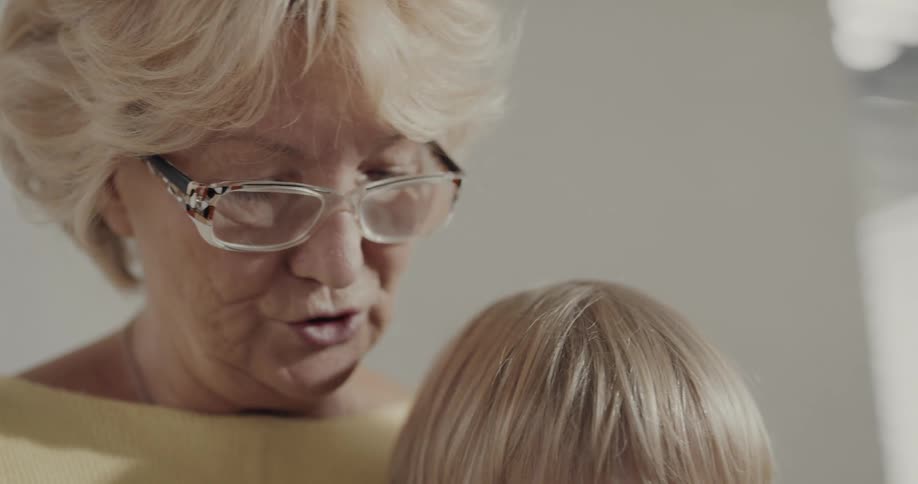 Grandmother wearing glasses reads to blonde grandchild