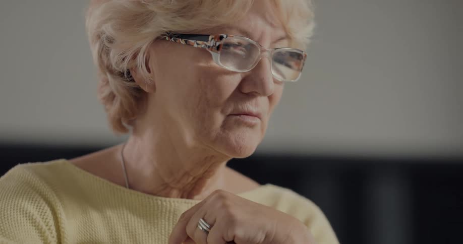 Female senior citizen sitting at a desk puts on reading glasses to work