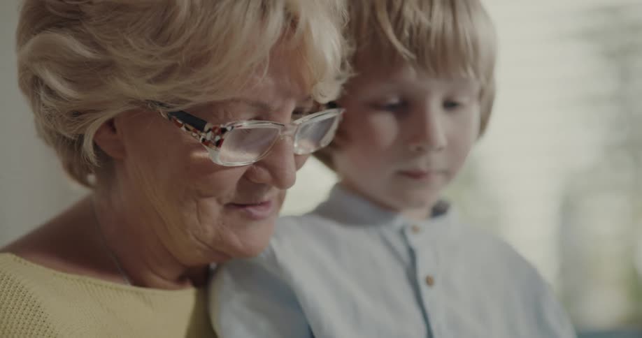 An elderly woman uses a computer tablet with the young boy sitting in her lap