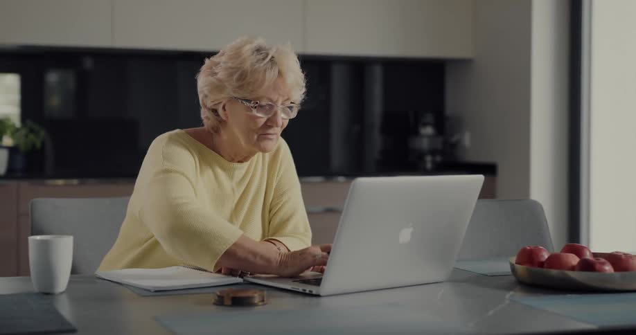 A woman is using a laptop and writing in a notebook