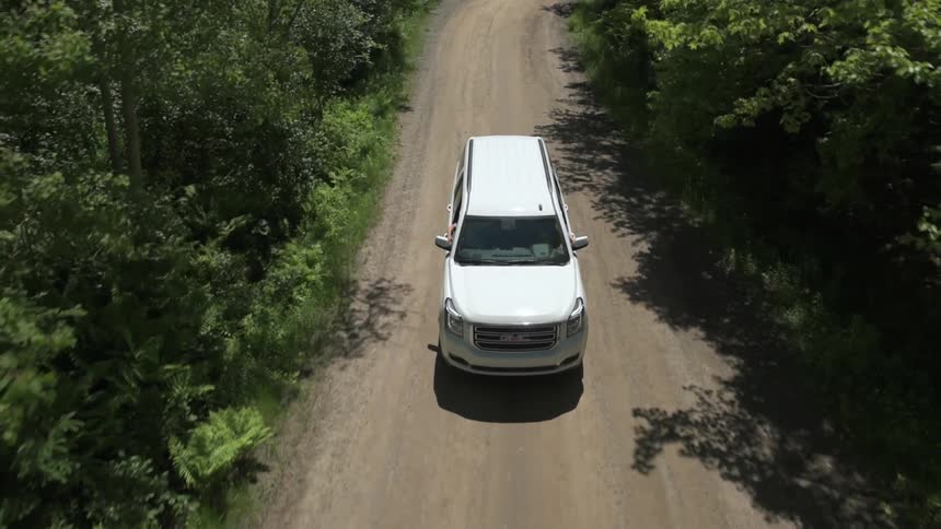 A white van travels on a tree lined rural road