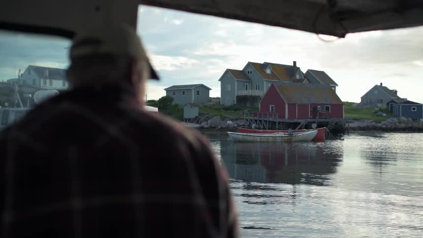 A man at the helm of a boat as it passes homes on shore