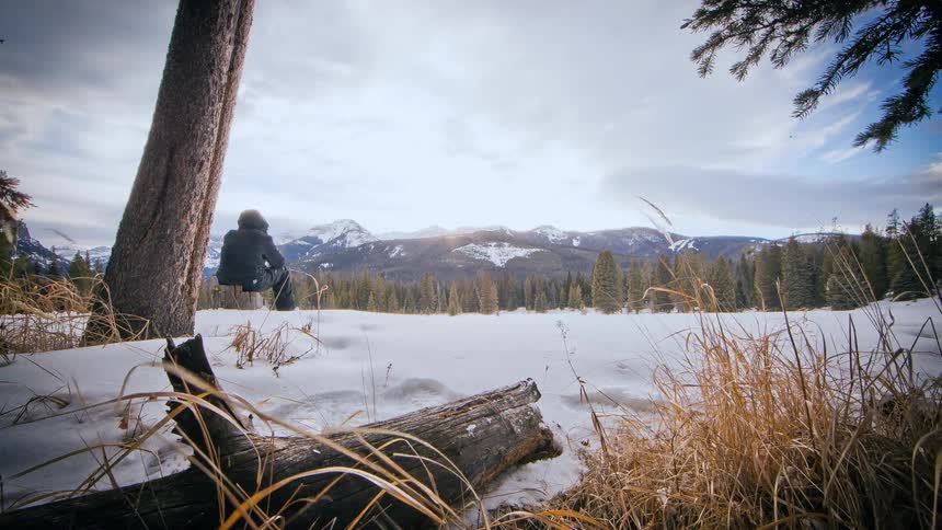 Clouds pass over a person overlooking a snowy mountain scene