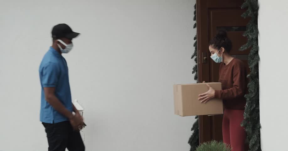 A woman exits a house just in time to be handed a packaged from a carrier