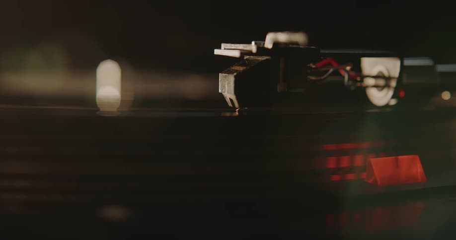 Close up of the arm of a turntable moving close to a spinning vinyl record