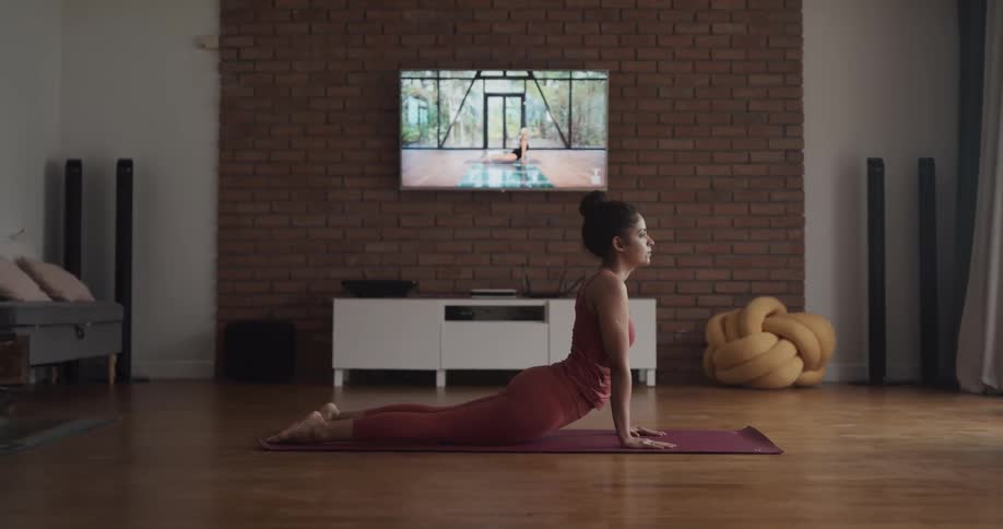 Young woman wearing sports clothes practices yoga over a mat at home