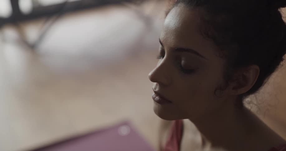 A woman meditates while sitting on a yoga mat indoors during the day