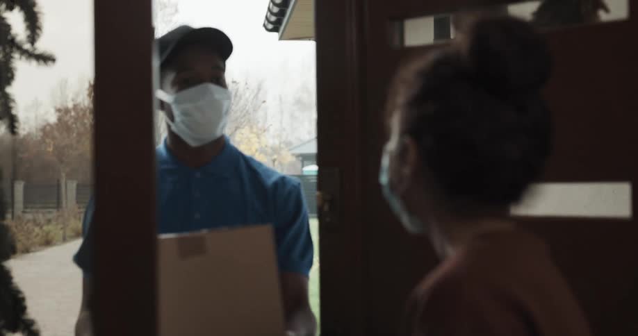 Woman wearing a face mask at home opens the door to receive a package delivery