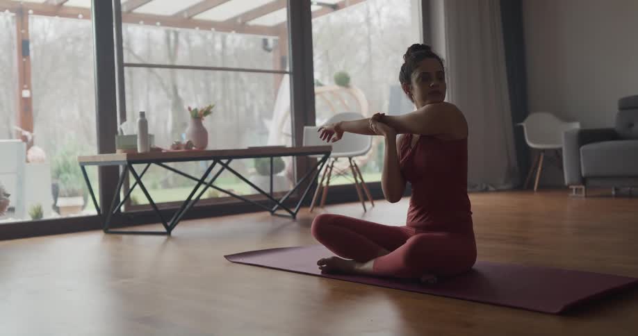 Female sitting on yoga mat stretching in living room