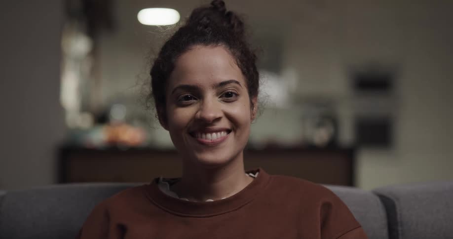 A woman is smiling and sitting on a couch indoors