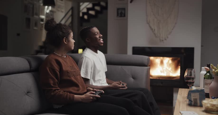 Young couple playing video games in the living room next to a roaring fireplace
