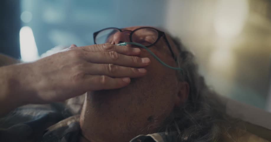 A man wearing an oxygen mask struggles to breathe while coughing on the couch
