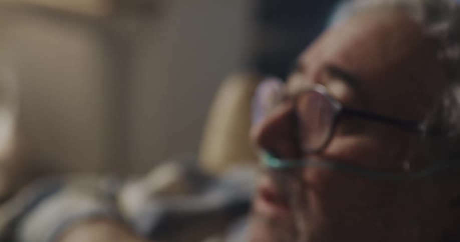 Sick man wearing a nasal canula have a coughing fit sitting on the couch at home