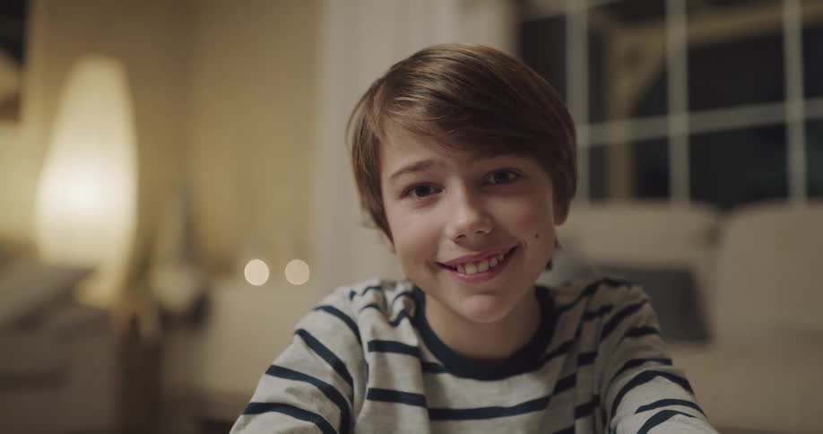 Young boy sitting in the living room at home looks at the camera smiling