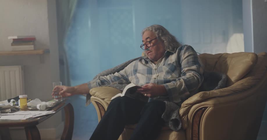A man is drinking a glass of water and reading a book