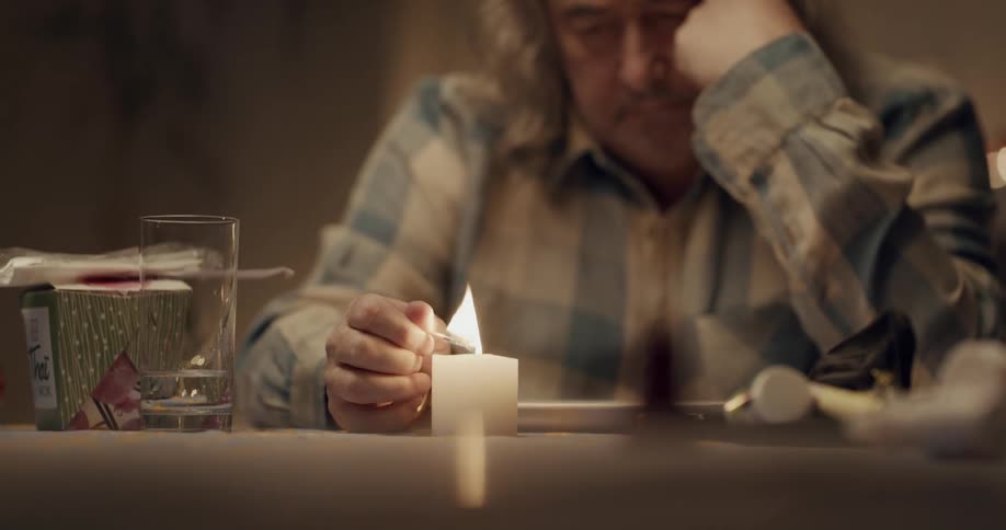 Mature man with long wavy hair lights a candle with a match over the table