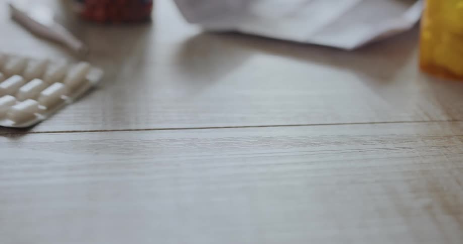 A woman slides a package of medication across a table at home