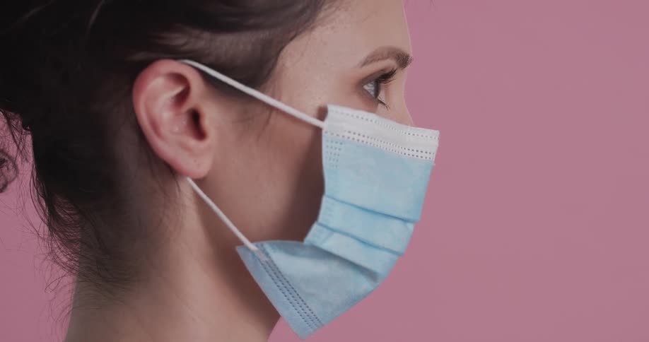 Side profile of female model with pink shirt putting on blue mask