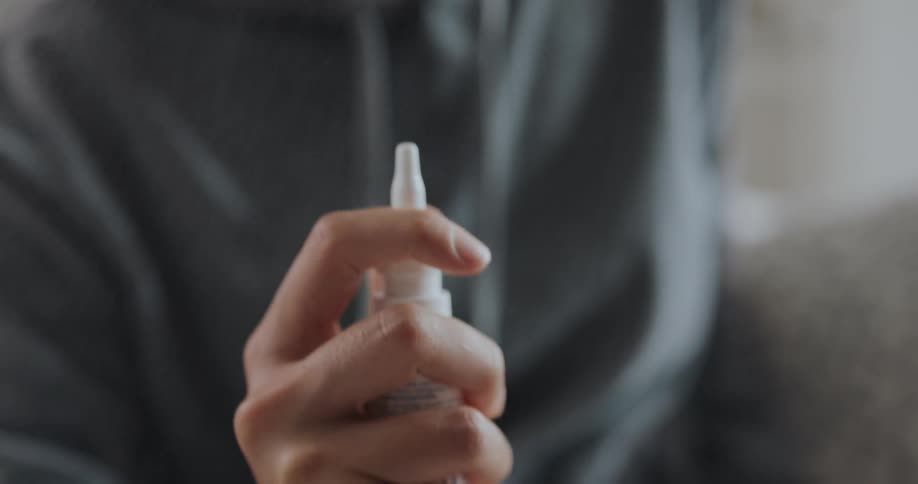 Sitting woman primes nasal spray before raising it toward her face