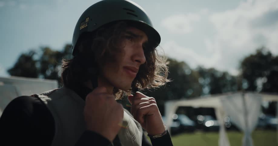 A man puts on a helmet while standing outdoors during the day