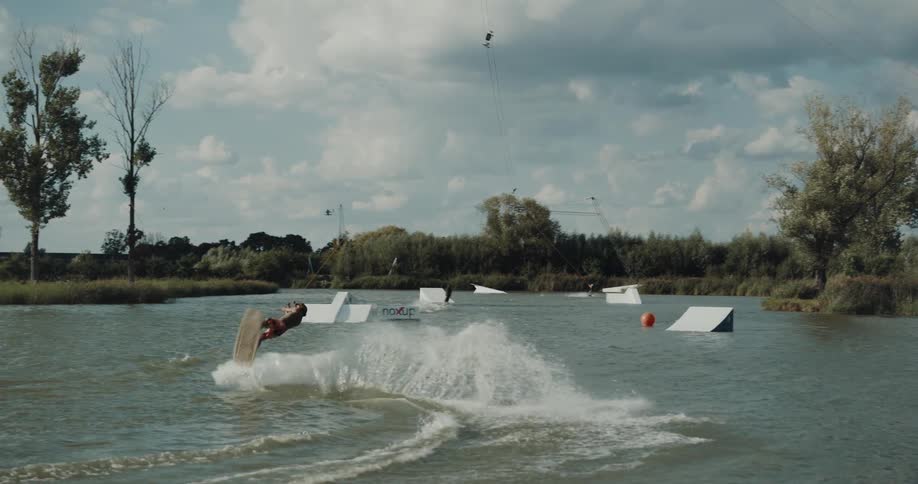 Young man rides a surfboard doing stunts on a lake pulled by a cable