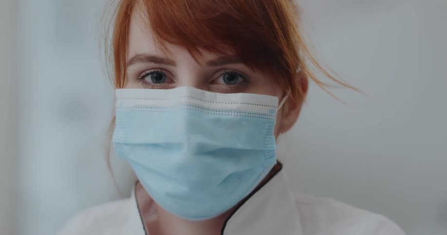 Close up of the face of a manicurist wearing a blue disposable face mask looking at the camera
