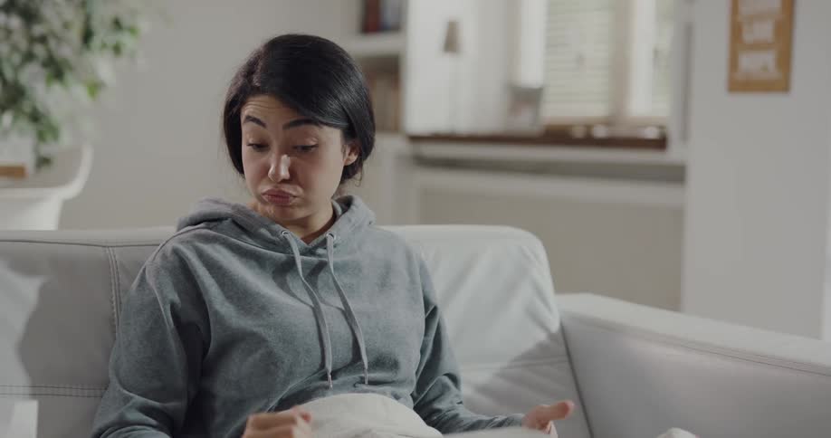 Sick woman sitting on a couch at home ends a video call on a laptop