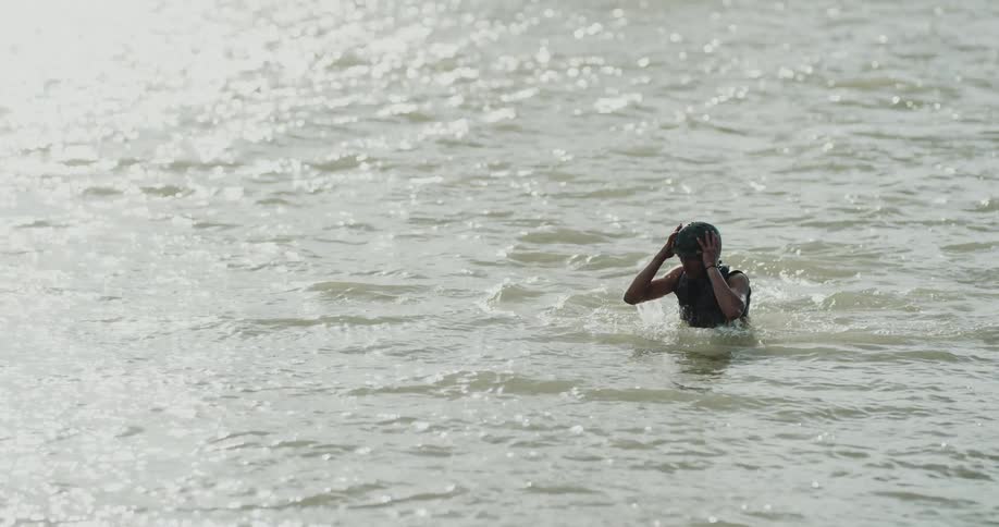 A man wearing a helmet does squats in a lake during the day