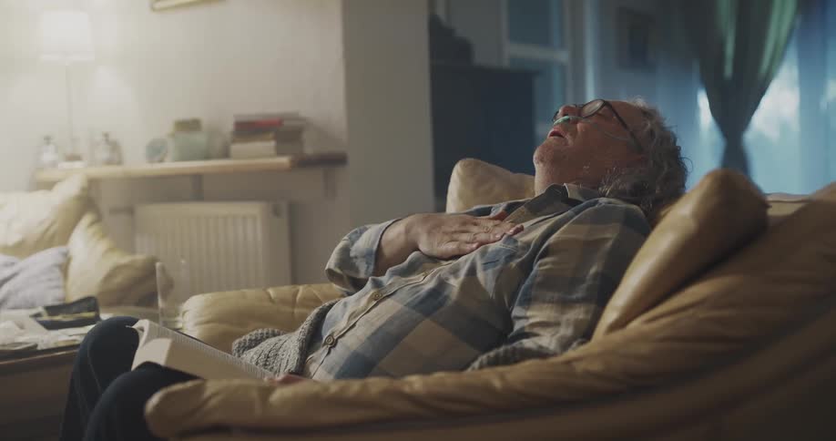 A man is sitting in his chair and reading a book while coughing