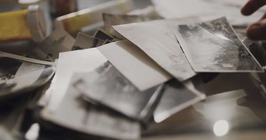 Man picks up black and white pictures from a coffee table surrounded by medicine containers