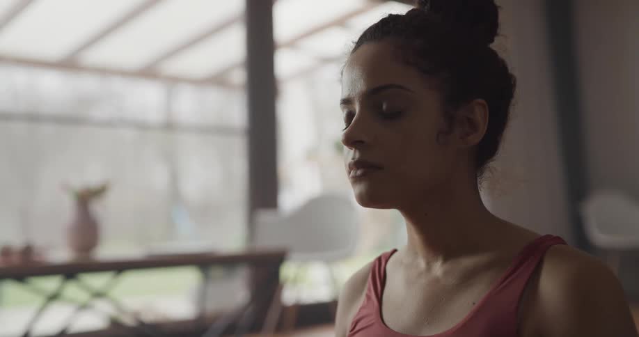 Young woman wearing sports clothes meditates sitting in the living room