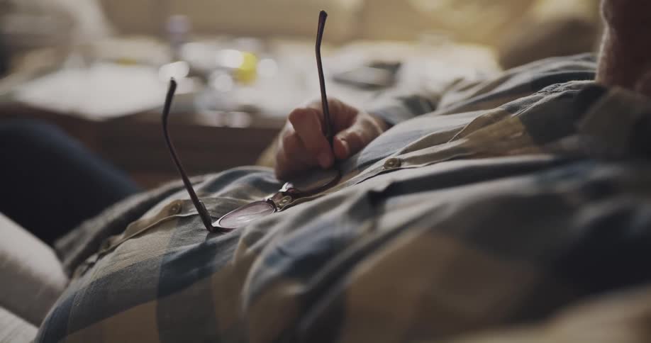 A man is holding his glasses against his chest while sleeping in a chair