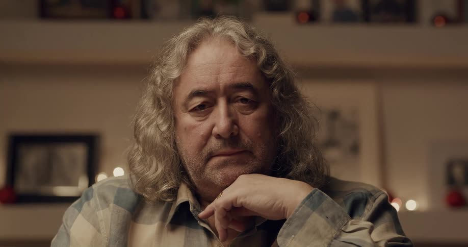 A man sits at home and rests his head on his hand as he looks ahead
