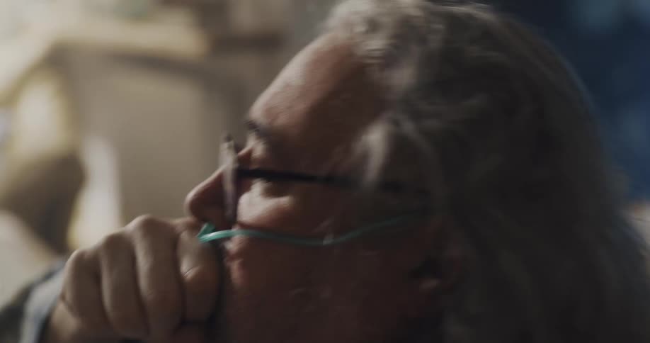 A man coughs and smacks his chest while struggling to breathe on the couch