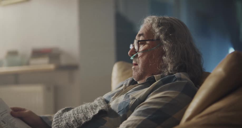 An older man coughing and reading a book