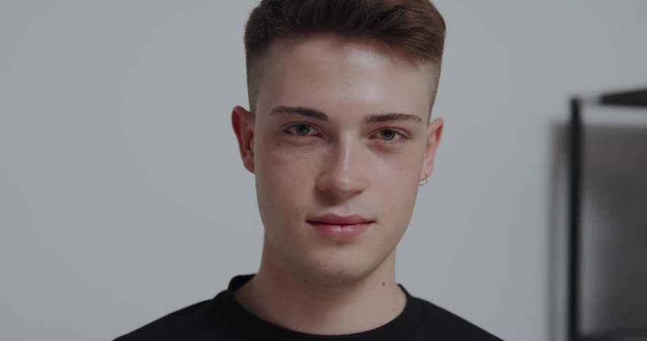 Man with earrings crew haircut and black t shirt smiles at camera