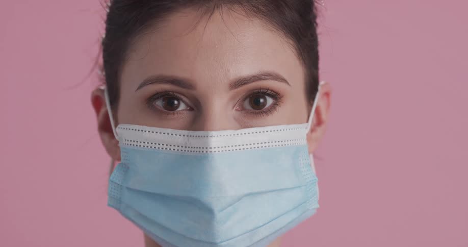 A woman looks straight ahead while putting on and adjusting a face mask