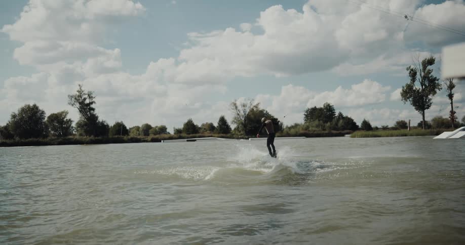Person wearing helmet cable water skis across rippling water toward the opposite shore
