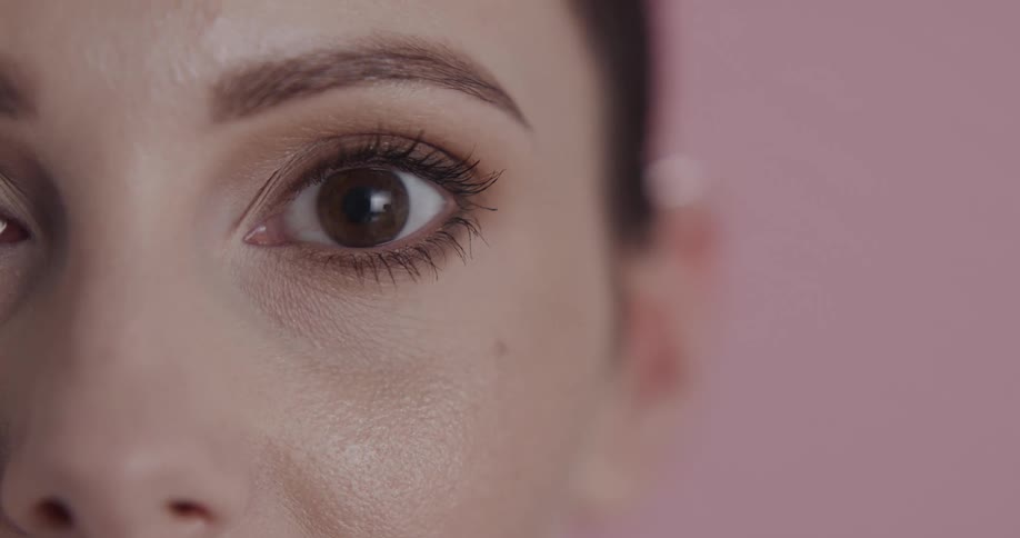 Close up of the eye of a woman standing in front of a pink background looking at the camera
