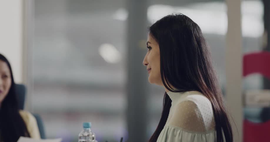 A woman speaks with her coworkers in a meeting in an office