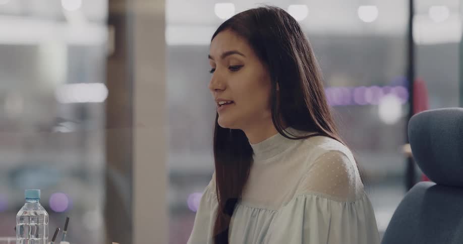 A woman talks to someone out of frame while sitting at a desk in an office