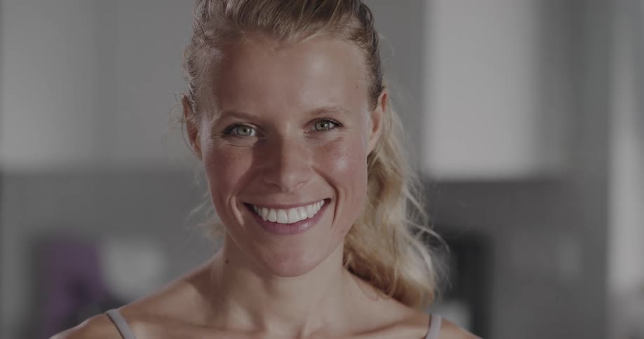 Blonde woman with ponytail and sports bra looks at camera