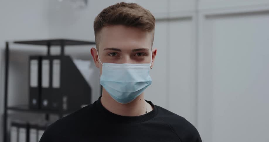 Young man wearing a blue disposable face mask looking at the camera