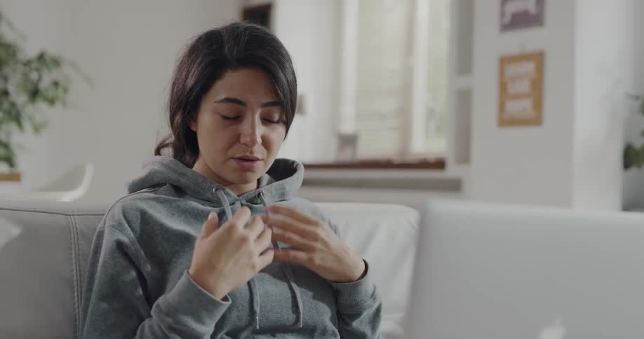 A woman is talking and sitting on a couch in the living room